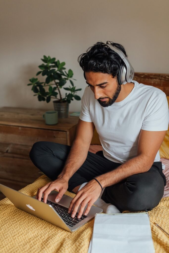 Young man with headphones working on a laptop in a home environment.